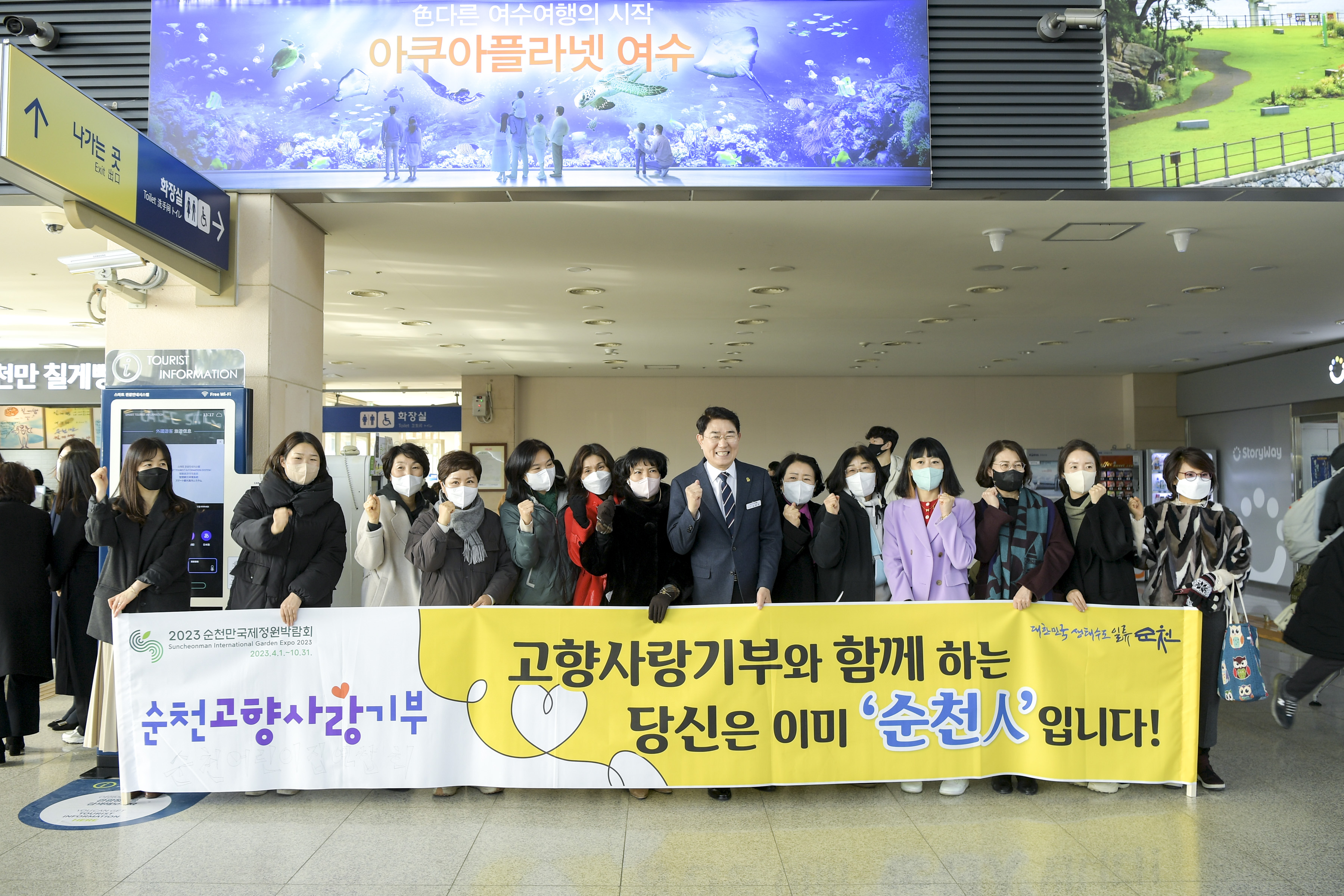 순천역에서 현수막(순천고향사랑기부 고향사랑기부와 함께하는 당신은 이미 순천人입니다)을 들고 있는 노관규 순천시장님과 여러명의 순천시민이 주먹을 쥐고 화이팅 하는 모습